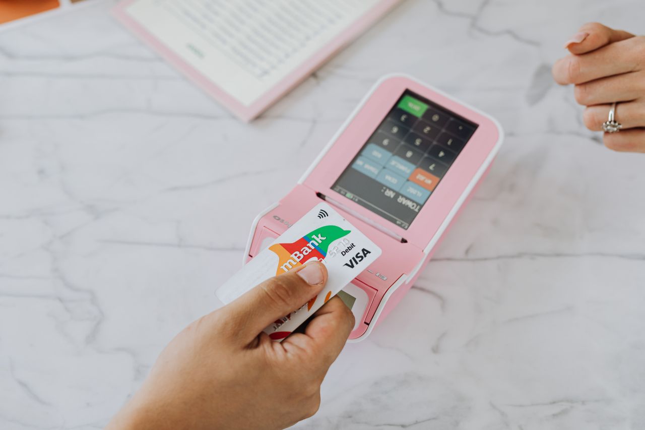 hero-img-02 Main tenant une carte sans contact sur un terminal POS rose pour une transaction sans fil.